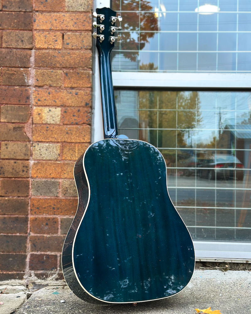 Blue acoustic guitar leaning against a brick wall with a window in the background