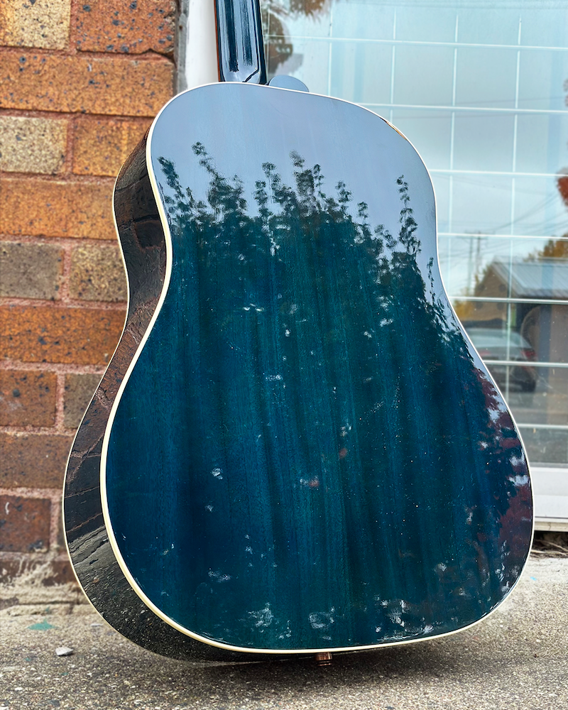 Blue acoustic guitar leaning against a building with a reflective surface.