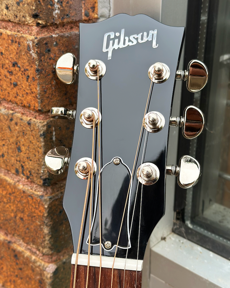 Gibson guitar headstock with tuning pegs against a brick wall.