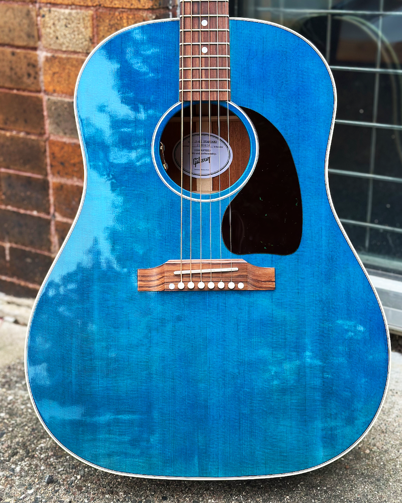 Blue acoustic guitar with a Gibson logo on a concrete surface.