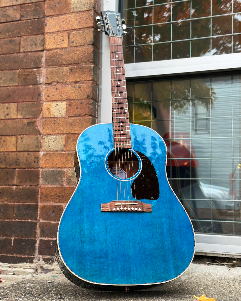 Blue acoustic guitar leaning against a brick wall with a window in the background